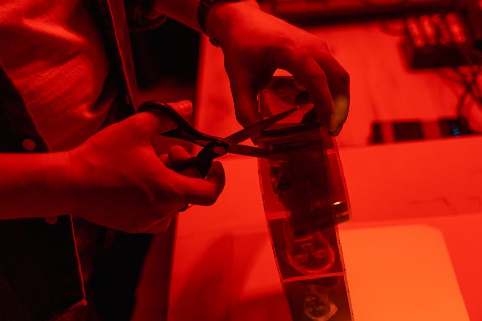 Close-up of a person cutting film negatives in a red-lit darkroom.